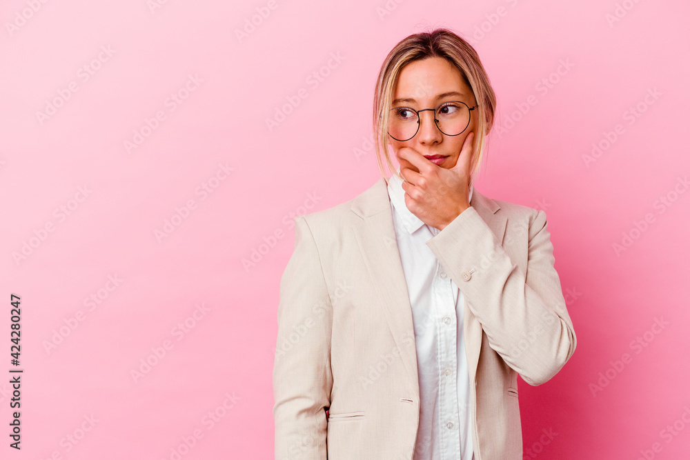 Young caucasian mixed race business woman isolated on pink background thoughtful looking to a copy space covering mouth with hand.