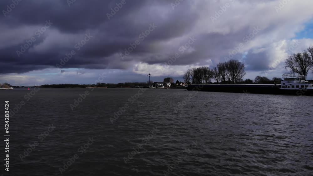 Rippling Water Of Oude Maas River In Puttershoek, Netherlands With Overcast. Flatboat Sailing On A Dramatic Weather. wide shot Rippling Water Of Oude Maas River In Puttershoek, Netherlands With Overcast. Flatboat Sailing On A Dramatic Weather. wide shot
