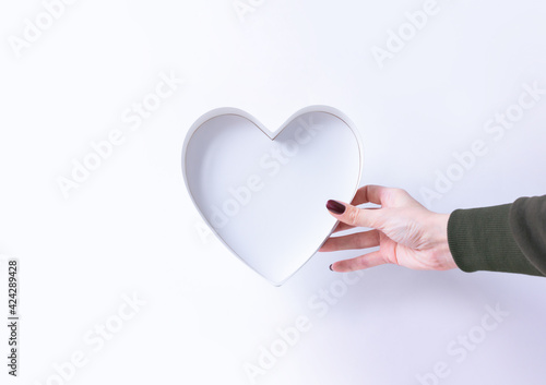 Hand holds a white blank heart-shaped box. Congratulations card for a holiday valentine's day, wedding, birthday, mother's day