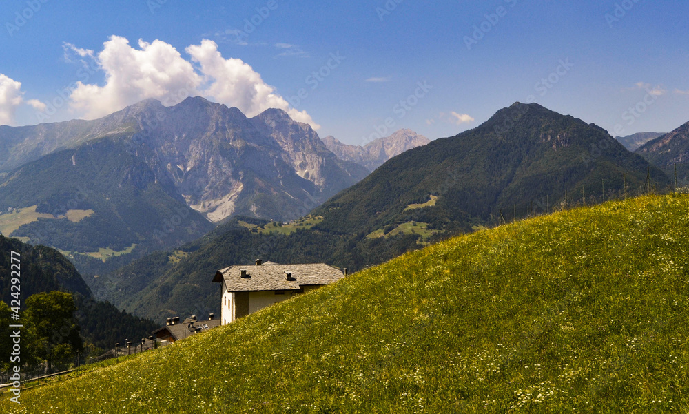 CASETTA AMONG THE MOUNTAINS AND GREEN MEADOWS WITH YELLOW FLOWERS AND THE BLUE SKY WITH WHITE CLOUDS