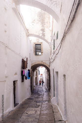 ALLEY OF A SMALL TOWN WITH WHITE WALLS AND FLOWERS ON THE BALCONIES AND STONE STAIRS © Adriana