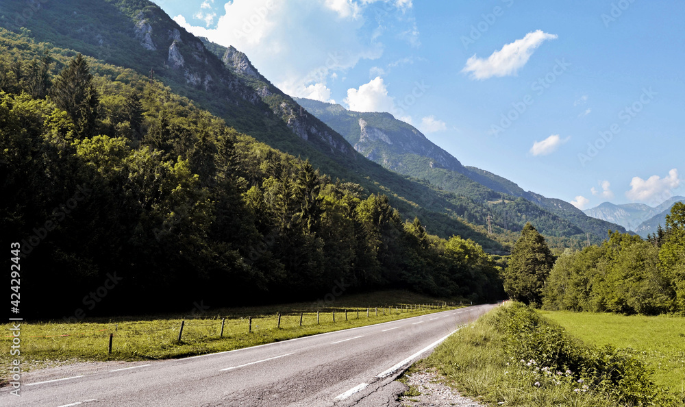 Naklejka premium LANDSCAPE AT SUNSET WITH WHITE CLOUDS WITH GREEN MEADOWS AND MOUNTAINS AND SMALL ROAD