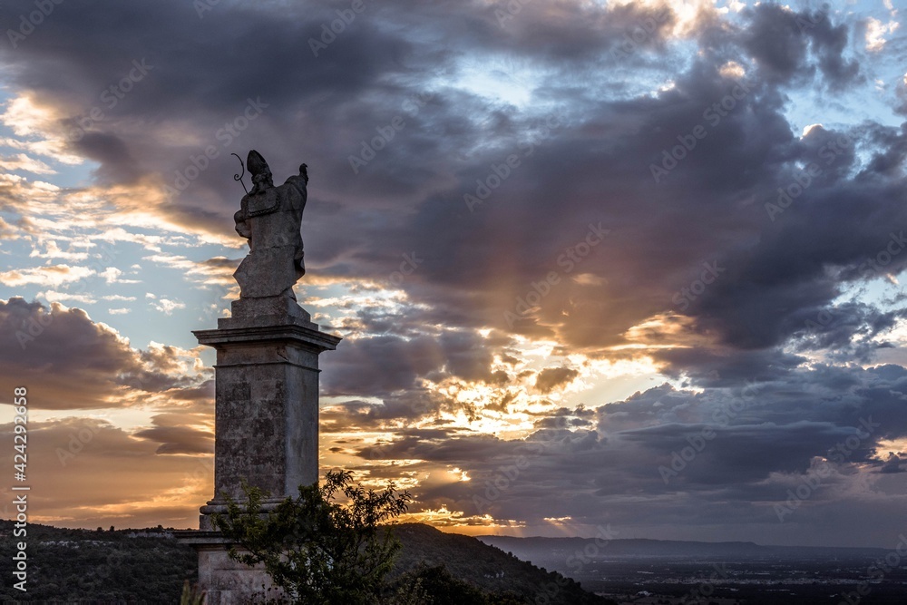 STATUE OF A SAINT PATRON LOOKING TOWARDS THE HILLS AND THE SUNSET