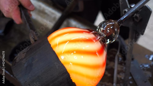 Glassblowing crafter rounds the hot-striped vase  with wet woode tool at the end of the glass blowing pipe. Traditional glass art workshop. Bohemia glass studio.