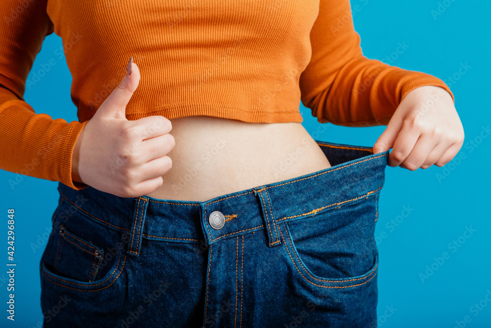 Skinny weight loss woman show flat stomach pulling by hands oversized big  blue pants jeans showing