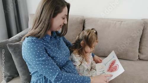 Little girl with pregnant mother drawing a picture at home