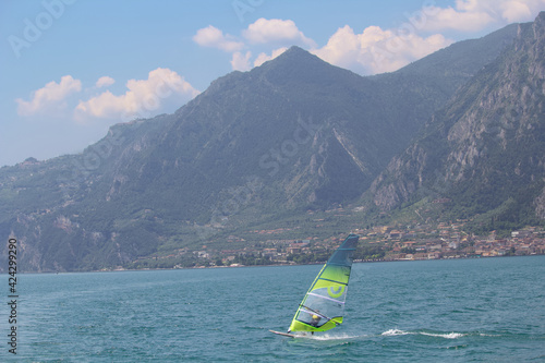 Windsurfer bei gutem Wetter im Vordergrund einer Bergkette mit Küstenort