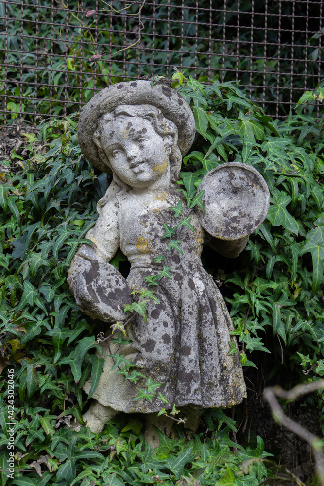 Old white weathered statue of a girl playing Clash cymbals surrounded with ivy Old white weathered statue of a girl playing Clash cymbals surrounded with ivy