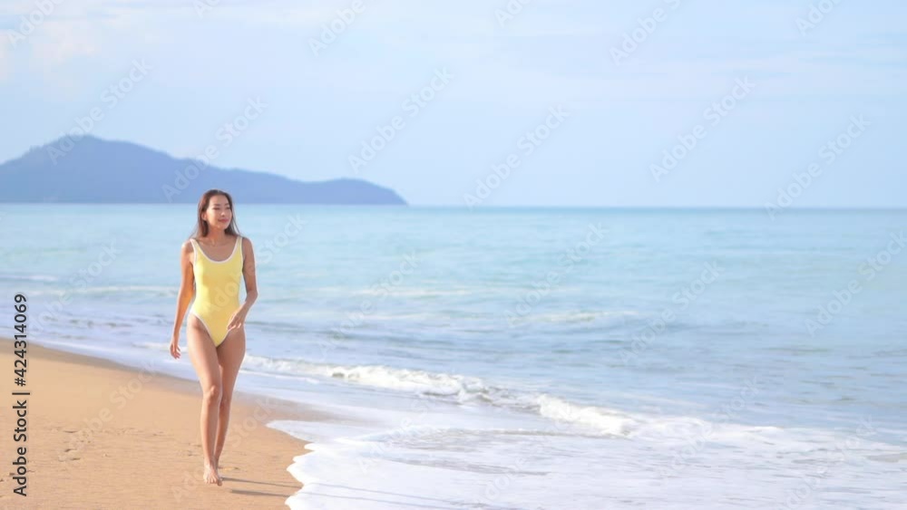 Lonely slim asian woman in swimsuit walking on sandy beach by tropical sea waves on sunny day, Lonely slim asian woman in swimsuit walking on sandy beach by tropical sea waves on sunny day,
