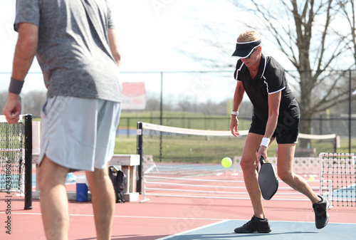 A senior woman hits a pickleball during a match.