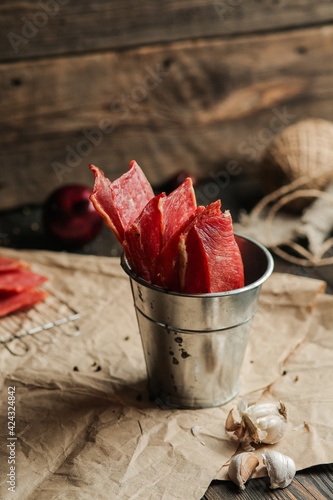 Homemade beef jerky seasoned with garlic, onion, pepper and salt. Jerky in a bucket on a wooden background