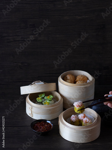 Assorted Dim Sum on Dark Background with copy space. Dim Sum Dark Food Photography. Shumai (Prawn and Pork meat dumplings) with Chopsticks. 