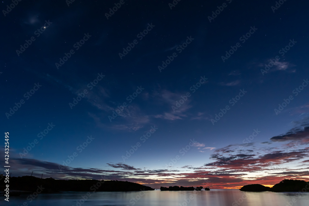 Beautiful and peaceful long exposure scene taken at the blue hour on Hoshizuna beach, calm sea, beautiful blue, yellow and orange color on horizon and some stars appearing on a dark blue sky. Beautiful and peaceful long exposure scene taken at the blue hour on Hoshizuna beach, calm sea, beautiful blue, yellow and orange color on horizon and some stars appearing on a dark blue sky.