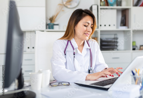 Woman doctor in uniform is working behind laptop in clinic