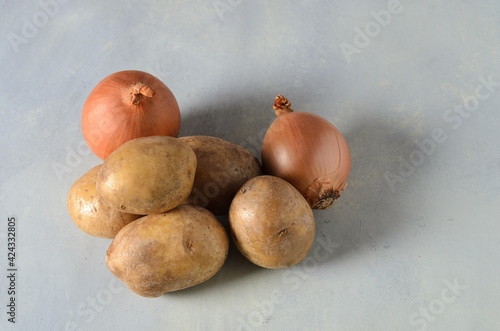 Potato tubers with onions and garlic on a textured yellow-gray background