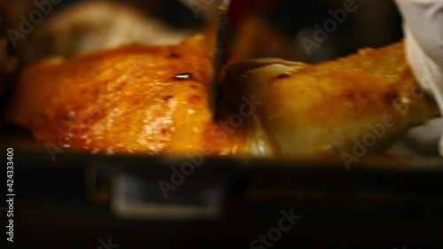 Female chef carves a big spatchcocked oven roasted chicken on a baking tray. Process of cooking shkmeruli - Georgian dish. Macro view photo