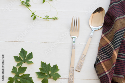 spoon and fork for eat a foods with leaves and cloth arrangement flat lay postcard style on background white wooden
