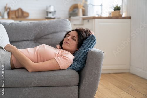 Young woman with closed eyes lying on pillow, resting, trying to sleep in uncomfortable pose on sofa at home, feel fatigue. Tired girl fall asleep, taking nap. 