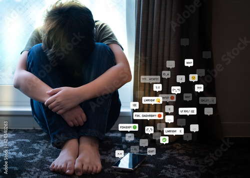 Cyberbullying - social media harassment concept. Young asian preteen, teenager boy sitting alone in the room feeling frustrated after reading bad comments. Text emoticons, Teen mental health, Online. photo