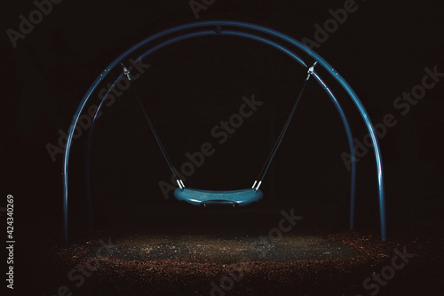 Playground at night, a surreal and eerie photo. Illuminated Swing. Concept of Isolation, Loneliness and Sadness.