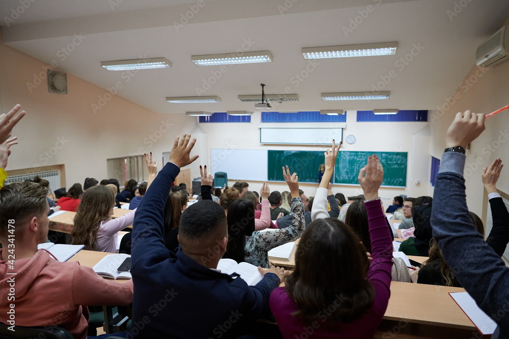 Fototapeta premium Raised hands and arms of large group of people in class room