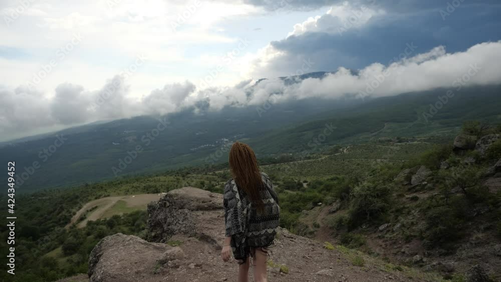 A young female traveller in short black shorts and sports boots climbs up a hill, with panoramic views of the mountain valley and clouds. High quality FullHD footage A young female traveller in short black shorts and sports boots climbs up a hill, with panoramic views of the mountain valley and clouds. High quality FullHD footage