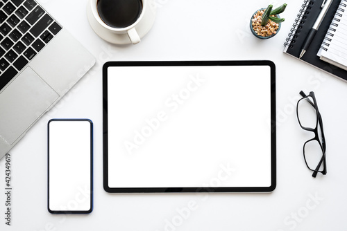 Desk white workspace with tablet a smartphone blank white screen and laptop computer is placed at the office. Mock up.