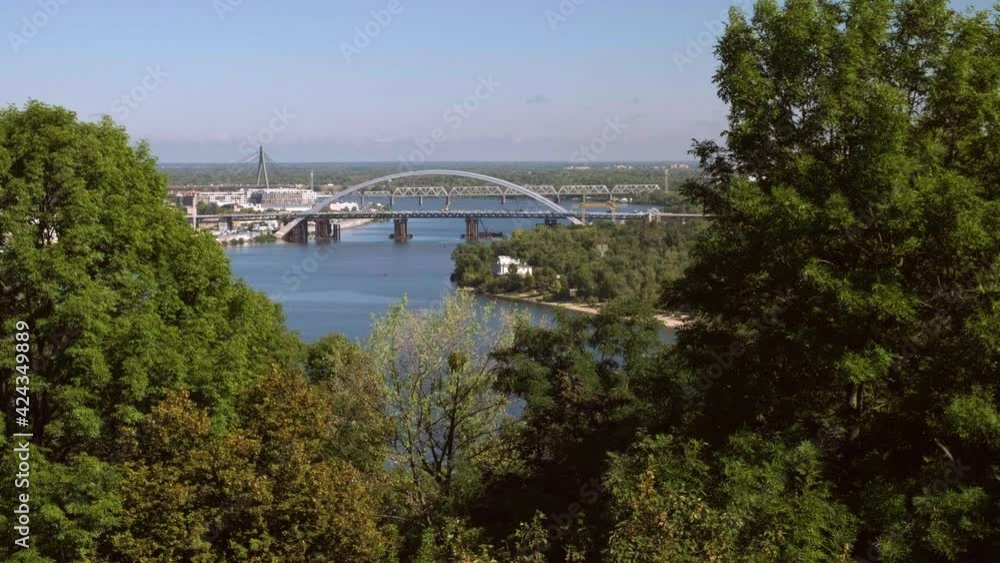 Long clip of the Podilskyi Bridge over Dnieper River in Kiev. Shot from Volodymyrska park, framed by trees Long clip of the Podilskyi Bridge over Dnieper River in Kiev. Shot from Volodymyrska park, framed by trees
