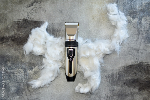 Hair trimmer and white animal fur. wool is laid out in shape of cat. Working tool, pet care, haircut cat. bunch of cat hair after grooming in form of cat. removal of cess animal hair during molting. photo