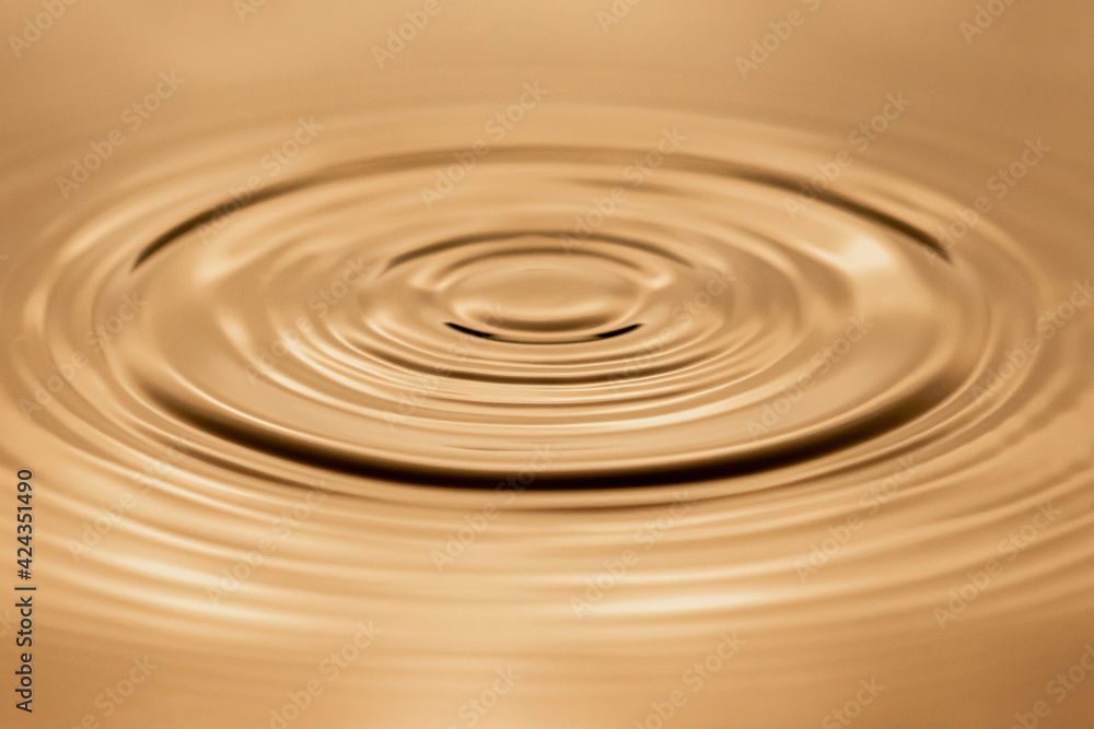 Water droplet dripping into golden pool creating ripples and abstract shape of water. Image contains some grain, noise and motion blur Water droplet dripping into golden pool creating ripples and abstract shape of water. Image contains some grain, noise and motion blur