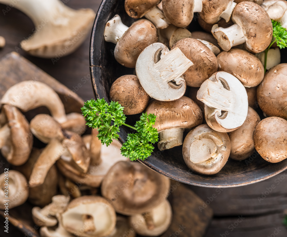 Fototapeta premium Different brown colored edible mushrooms on wooden table with herbs. Top view.