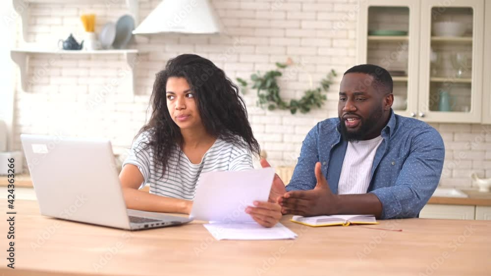 Worried multiracial couple looking through utility bills sitting with a laptop at the table in the kitchen, concerned African man and woman arguing because of have not enough money in the account Worried multiracial couple looking through utility bills sitting with a laptop at the table in the kitchen, concerned African man and woman arguing because of have not enough money in the account