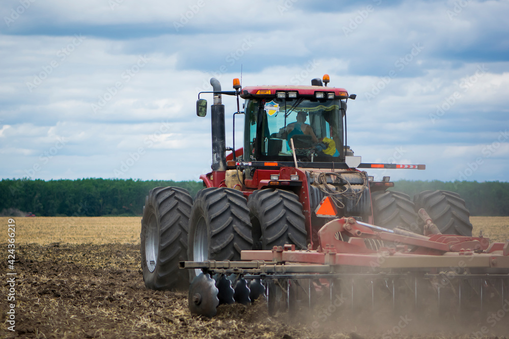 Fototapeta premium red tractor in a field rear view, tractor with a plow on an agricultural field. big red tractor working in the field, harvesting, business, agriculture. August, Kiev region