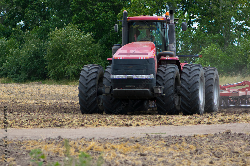Red tractor with a plow on an agricultural field. work in the field with a big red tractor close-up, harvesting, farming. august 2020 Ukraine, Kiev region Red tractor with a plow on an agricultural field. work in the field with a big red tractor close-up, harvesting, farming. august 2020 Ukraine, Kiev region