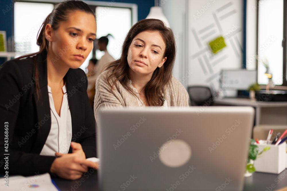 Close up of diverse businesswomen checking graphs from laptop making new strategy for start up business. Manager explaining to colleagues new financial project sitting at desk in startup office Close up of diverse businesswomen checking graphs from laptop making new strategy for start up business. Manager explaining to colleagues new financial project sitting at desk in startup office