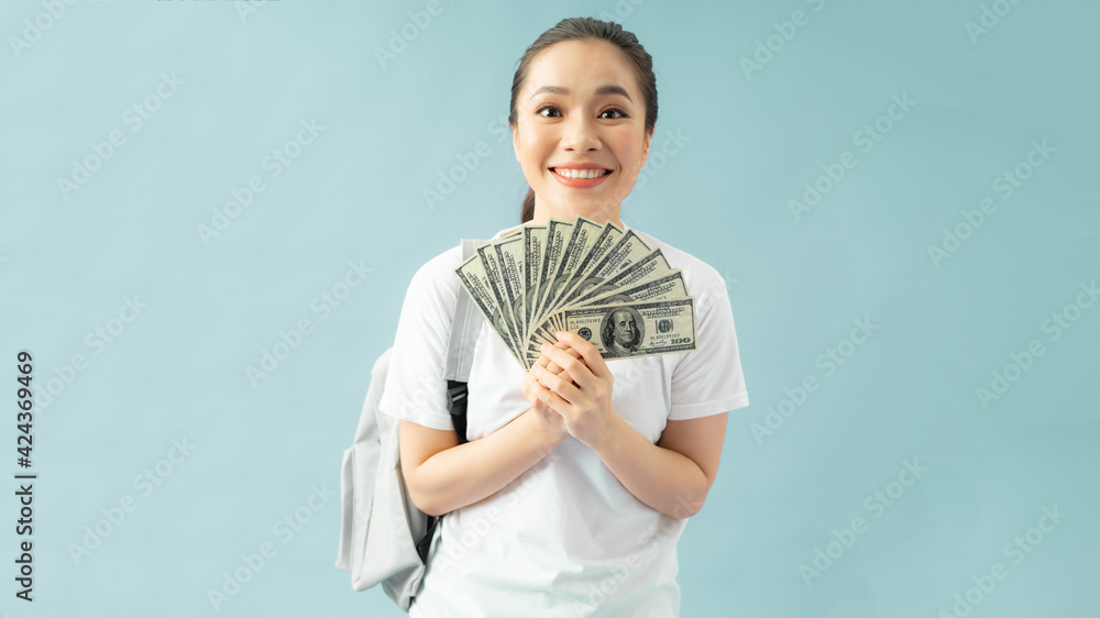 Shocked girl student in backpack isolated on pastel blue background, hold fan of cash money in dollar banknotes put hand on cheek Shocked girl student in backpack isolated on pastel blue background, hold fan of cash money in dollar banknotes put hand on cheek