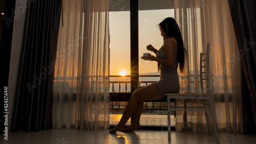 A woman sitting in the evening drinking coffee reams of the window that shines brightly.