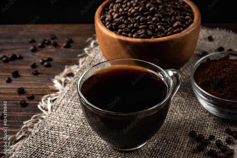 Cup of coffee with coffee beans and powder on dark wooden background Cup of coffee with coffee beans and powder on dark wooden background