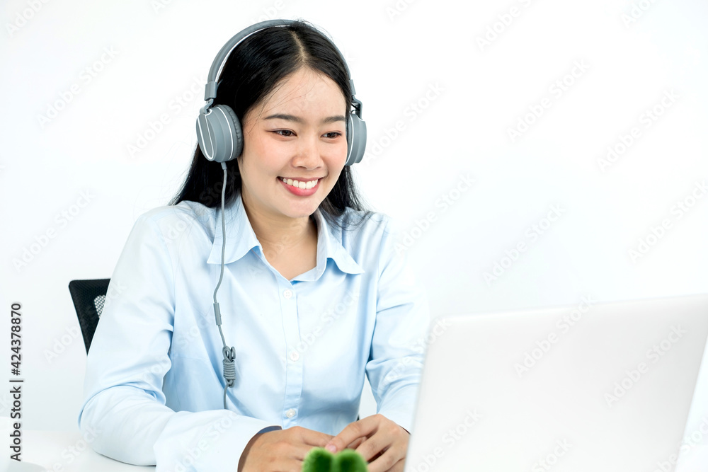 Video call, a young Asian woman wearing headphones, communicates via online video long distance, looking at the digital laptop screen, happily greeted with a friend Video call, a young Asian woman wearing headphones, communicates via online video long distance, looking at the digital laptop screen, happily greeted with a friend