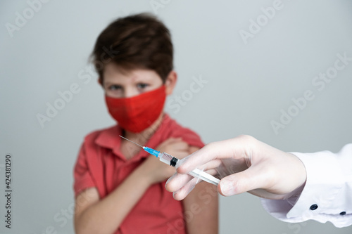 A child in a medical mask is vaccinated against the coronavirus in the covid pandemic. Doctor in medical gloves with a syringe makes an injection. photo