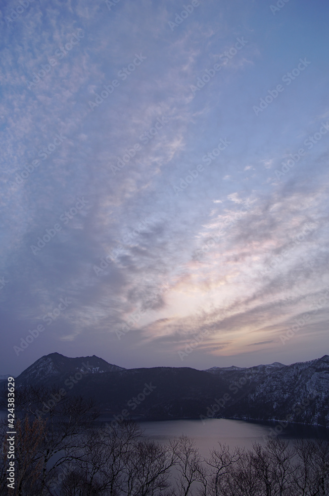薄い雲の広がる夜明けの空と山間の湖。日本の北海道の摩周湖。 薄い雲の広がる夜明けの空と山間の湖。日本の北海道の摩周湖。