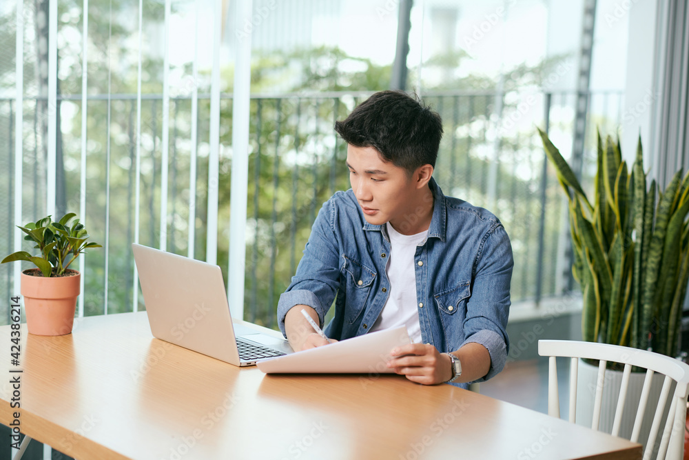 Fototapeta premium Rear view of a journalist stylish guy writing a story in a workplace in loft styled coworking, well dressed, sitting near window with view of garden