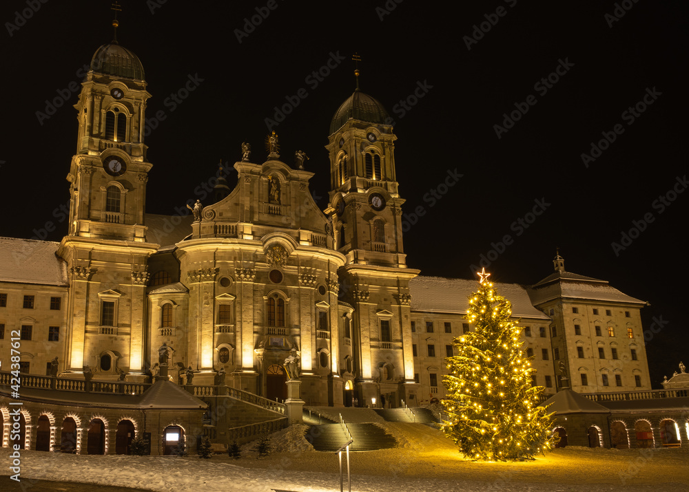The Benedictine Abbey of Einsiedeln with its mighty basilica is the main catholic pilgrimage center in Switzerland. Christmas tree and snowy winter night.