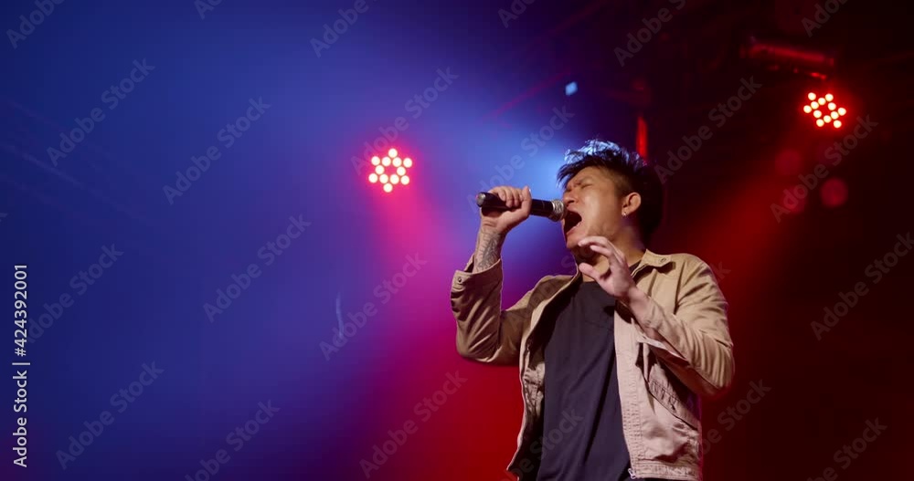 Asian vocal rock star band musician performing in stage in night club with spotlight and colorful laser ray. Singer playing to the crowd audience on music festival indoor concert Asian vocal rock star band musician performing in stage in night club with spotlight and colorful laser ray. Singer playing to the crowd audience on music festival indoor concert
