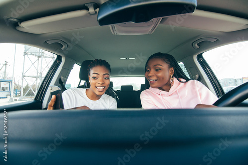 Two young african woman use phones in the car while driving car on the road