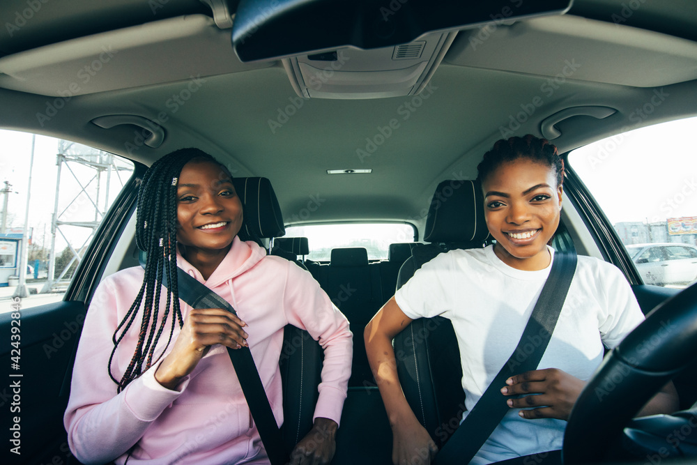 Beautiful young african women is fastening seat belts and smiling while travelling by car
