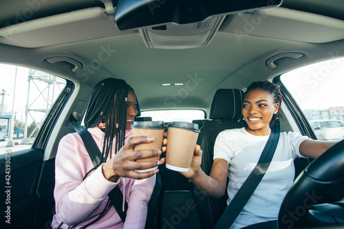 Happy african women friends with cup of coffee in car. Holiday trip of friends