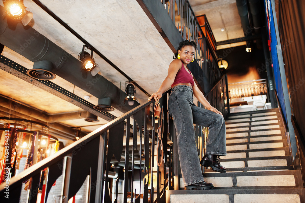 African woman in red marsala top and jeans posed indoor. African woman in red marsala top and jeans posed indoor.
