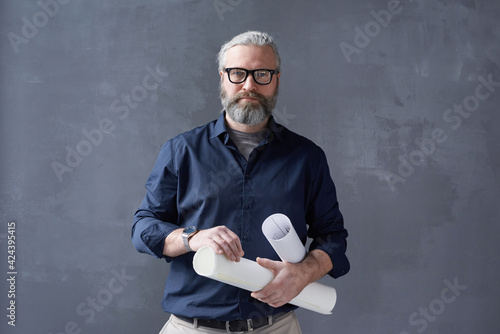 Portrait of mature bearded architect in eyeglasses standing with blueprints against the black background photo