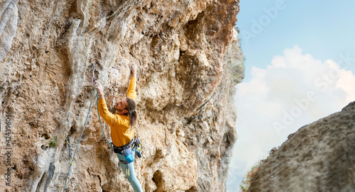 sports man climber climbing on the rock route, making hard move and cliping rope